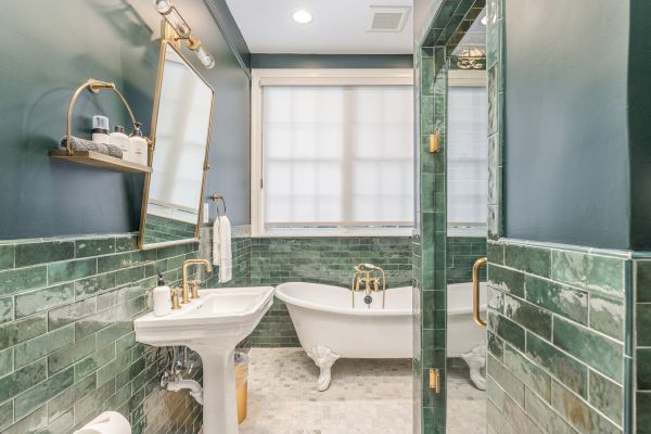 A bathroom with green subway tiles, a freestanding bathtub, a pedestal sink, a mirror, and gold fixtures, all creating a stylish look.