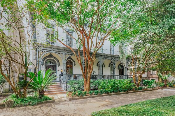 A charming, historic building with ornate details, surrounded by lush greenery and trees, featuring arched windows and a welcoming front porch.