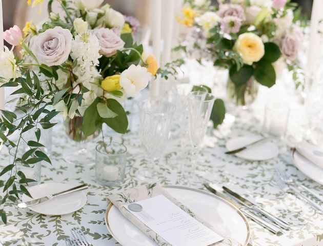 A beautifully set table adorned with floral arrangements, white plates, cutlery, menus, and glassware on a patterned tablecloth.